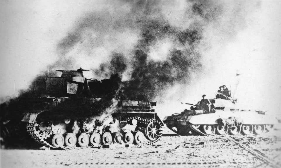 A British Crusader tank passes a burning German Pzkw Mk IV during Operation Crusader, November 1941 NAM. 2002-08-13-7 National Army Museum, Out of Copyright